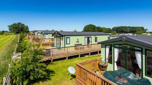 Lush green holiday park with cabins on wooden decks, surrounded by fields under a clear blue sky.