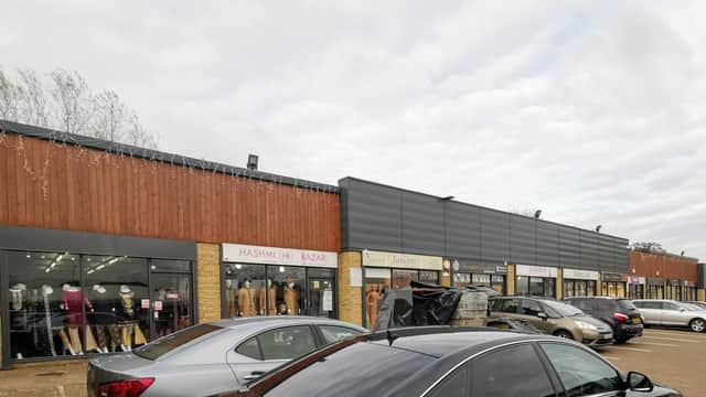 Shopping center exterior with shops, parked cars, and cloudy sky in Bradford, Yorkshire.