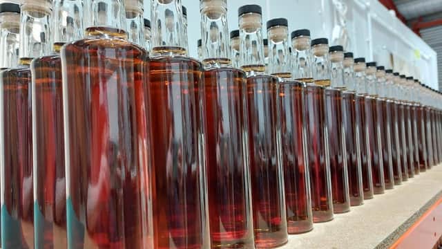 Rows of glass bottles filled with amber liquid, lined up on a shelf in a distillery setting.