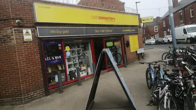 Jewellery shop with a sign reading "We buy gold," surrounded by bicycles and barbed wire on the building.