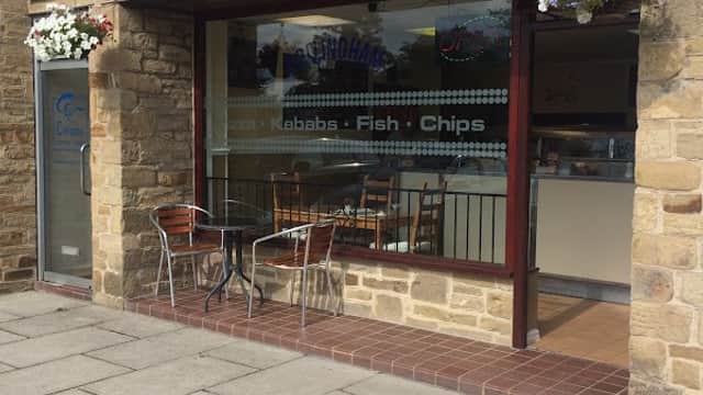 Restaurant exterior featuring a sign for "Pizza, Fish & Chips," with outdoor seating and stone facade in Collingham.