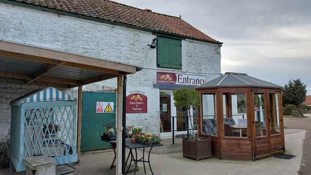Quaint stone building with green door, sign for bakery, and outdoor seating area with flowers in Potter Brompton, Yorkshire.
