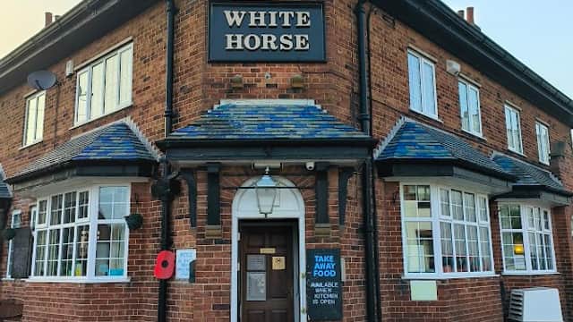 Historic brick bar with a sign reading "White Horse," featuring outdoor seating and a poppy wreath.