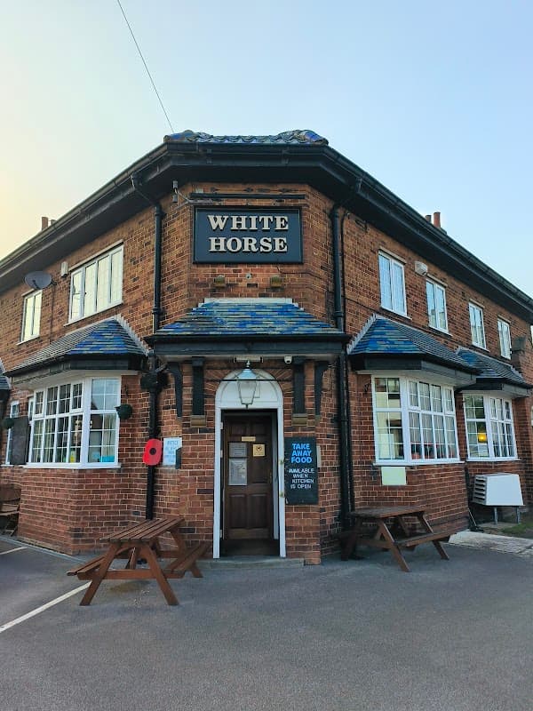 Historic brick bar with a sign reading "White Horse," featuring outdoor seating and a poppy wreath.