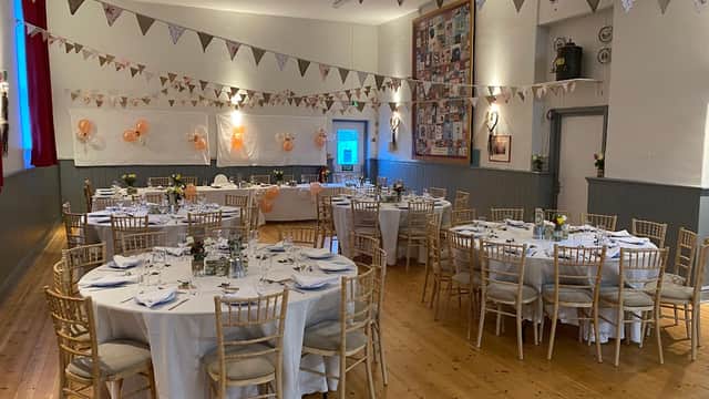 Decorated event space with round tables, chairs, bunting, and floral centerpieces, set for a celebration.