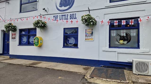 The Little Bull pub in Middlestown, Yorkshire, features blue windows, flower baskets, and English flags.