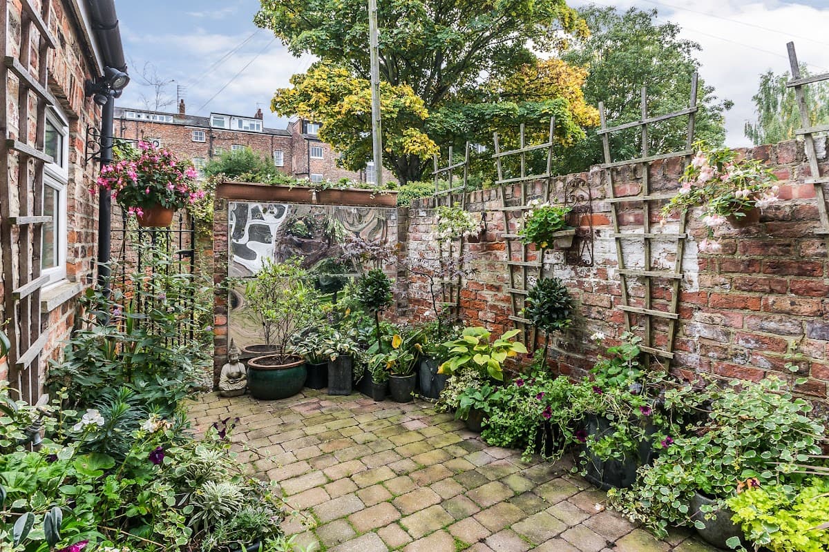 Lush garden with potted plants, brick walls, and trellises, creating a cozy outdoor space at St. Raphael Guest House.