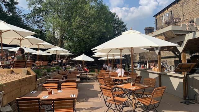 Outdoor bar area at The Malthouse in Rishworth, featuring wooden tables, umbrellas, and lush greenery.