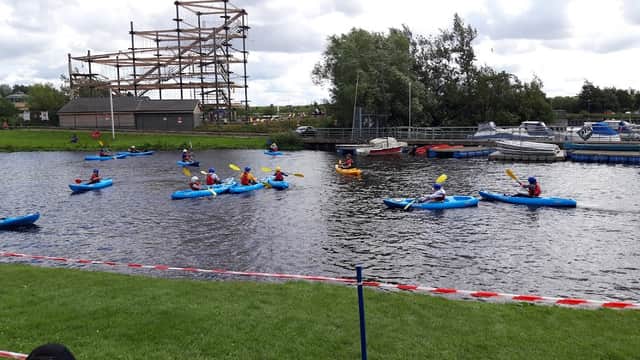 Kayakers on a river at Tees Barrage, with a construction site and trees in the background.