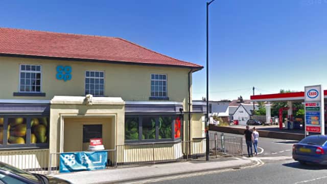 Co-op store with a red roof, adjacent to a petrol station, under a clear blue sky in Killinghall, Yorkshire.