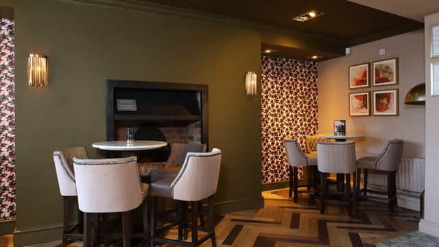 Cozy pub interior featuring a brick fireplace, floral wallpaper, and stylish seating arrangements.