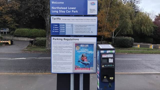 Sign for Northstead Lower Long Stay Car Park with parking tariffs and regulations, near trees and a pay machine.