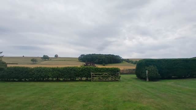 Lush green lawn with hedges and a wooden gate, overlooking rolling hills under a cloudy sky in North Yorkshire.