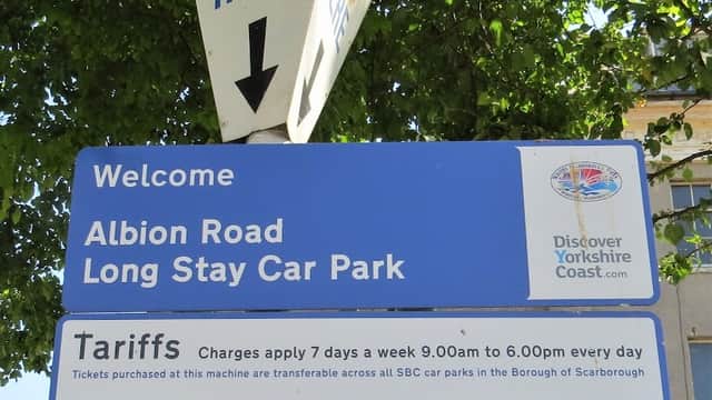 Sign for Albion Road Long Stay Car Park in Scarborough, detailing tariffs and payment instructions under a leafy tree.