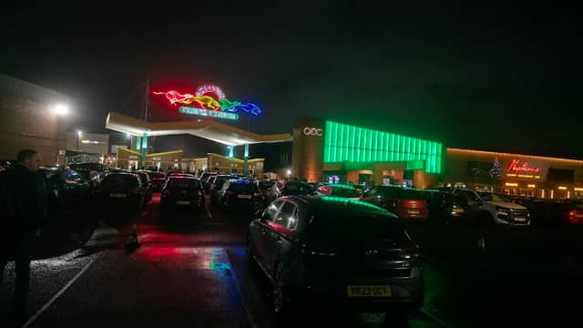 Brightly lit "Box of Dreams" sign with colorful neon, busy parking lot, and modern buildings under a night sky.
