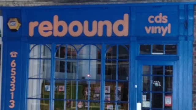Bright blue storefront of "Rebound" music shop, featuring large windows and signage for CDs and vinyl.