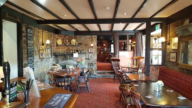 Cozy restaurant interior with wooden beams, stone walls, tables, chairs, and a fireplace, creating a warm atmosphere.