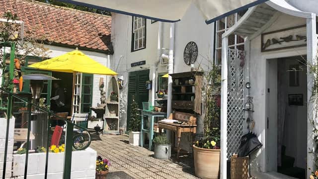 Quaint bar entrance with a sunny courtyard, yellow umbrellas, potted plants, and rustic decor in Crathorne, North Yorkshire.