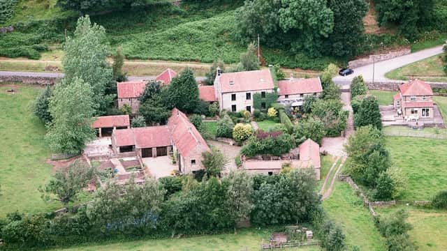 Aerial view of Red House Farm featuring several buildings, lush greenery, and a winding road in Glaisdale, Yorkshire.