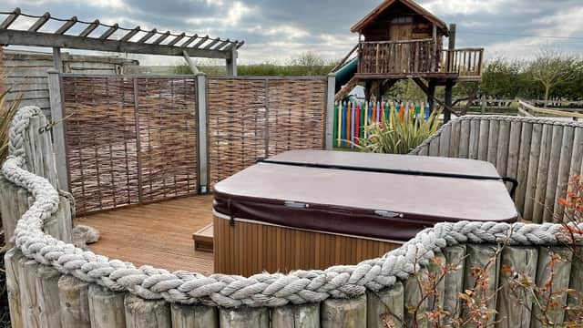 Hot tub enclosed by wooden fencing, with a treehouse and slide in the background under a cloudy sky.