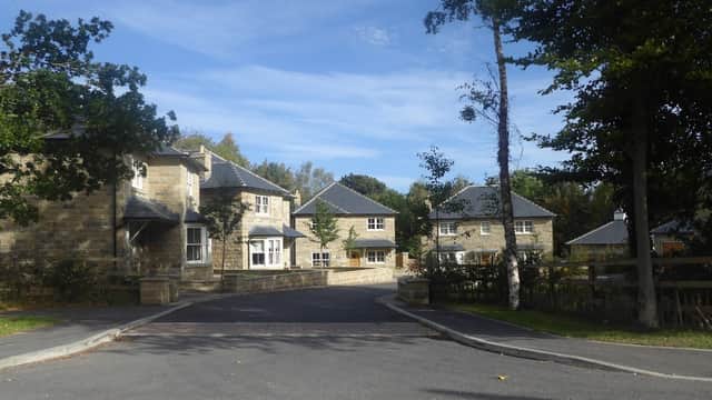 Stone buildings with slate roofs, surrounded by trees and a winding road in a rural setting.