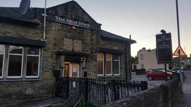 A stone building with large windows, a sign reading "The High Town," and a red car parked nearby.
