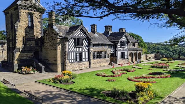 Historic building with black and white timber framing, surrounded by colorful flower gardens and lush greenery.