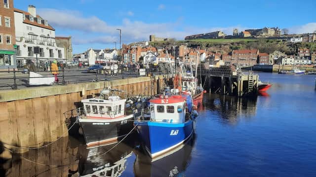 Colorful fishing boats docked in a calm harbor, with historic buildings and a hillside castle in the background.