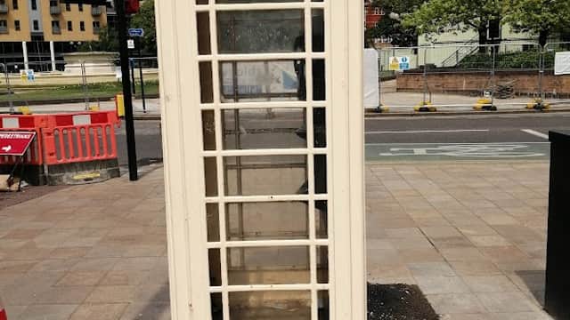 A vintage telephone booth stands on a sidewalk near a traffic signal and modern buildings in Hull, Yorkshire.