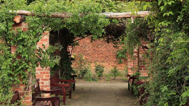 Overgrown archway with wooden benches, brick walls, and greenery in Thornes Park Stadium Car Park, Wakefield.