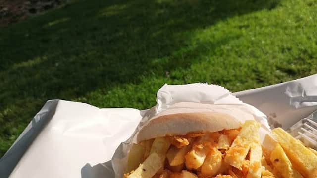 A serving of golden fries beside a bun, with a lush green park and stream in the background.