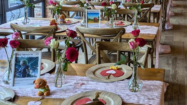 Tables set for a gathering, adorned with flowers, decorative plates, and small plush toys in a rustic, warmly lit setting.