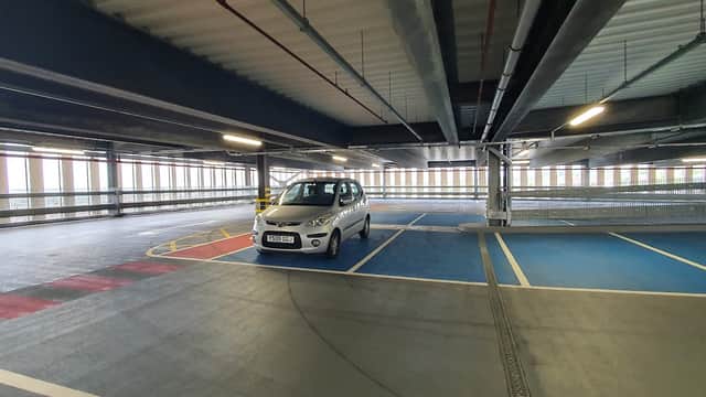 A spacious multi-level car park with a silver car parked in a blue bay and natural light streaming through windows.