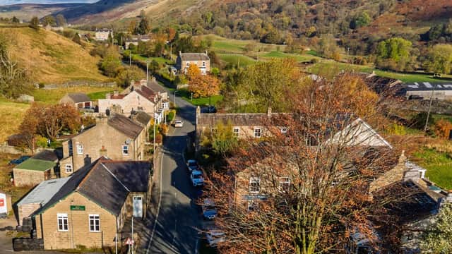 Reeth Memorial Hall nestled among stone buildings, surrounded by lush green hills and autumn-colored trees.