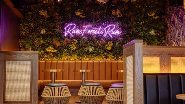 Cozy bar interior with tropical decor, neon sign, wooden seating, and stylish pendant lights.
