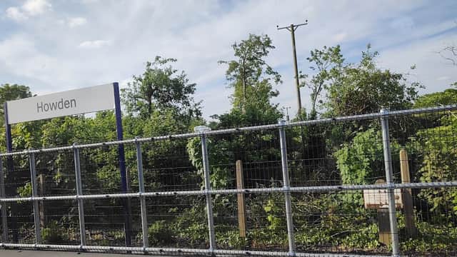 Sign for Howden with greenery and trees in the background, enclosed by a wire fence under a blue sky.