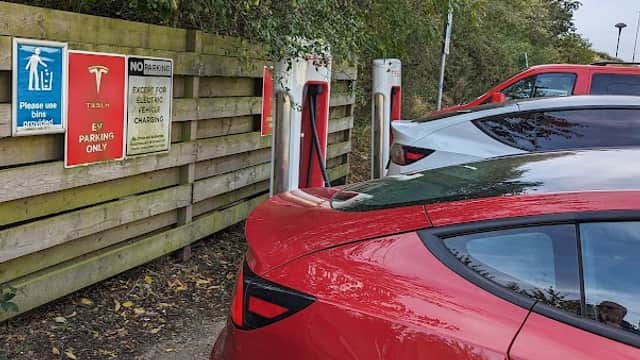 Tesla Supercharger station in Tingley, Yorkshire, with charging points and a red Tesla parked nearby.