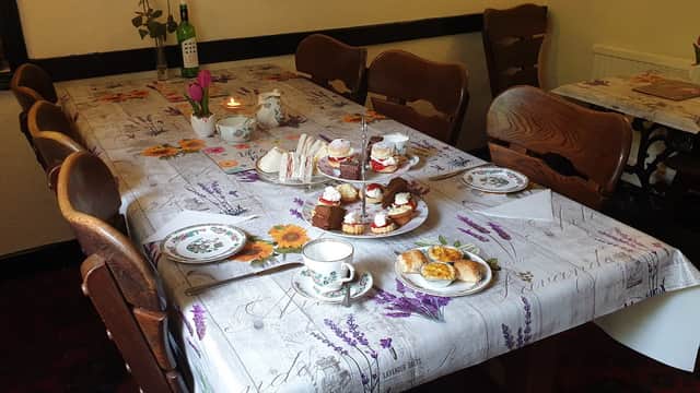 A dining table set with cakes, sandwiches, and tea, surrounded by wooden chairs in a cozy bar setting.