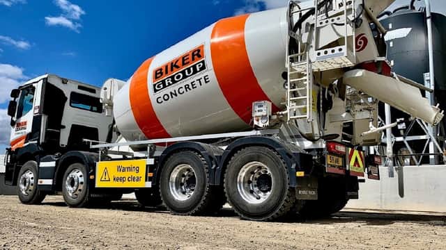 Concrete mixer truck with "Biker Group Concrete" branding, parked on gravel with warning signs visible.