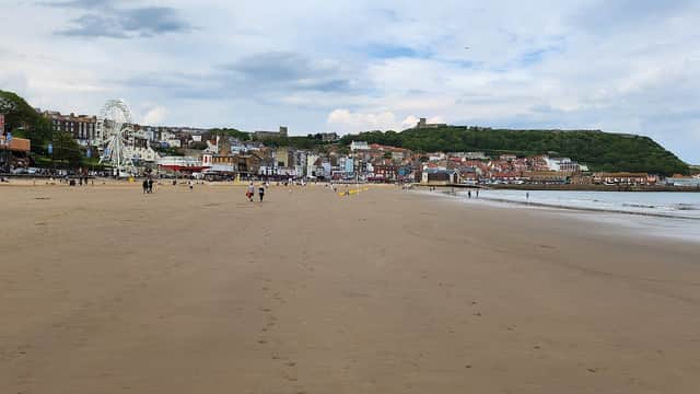 Beach scene with sandy shore, distant amusement rides, and Scarborough's coastal buildings under a cloudy sky.