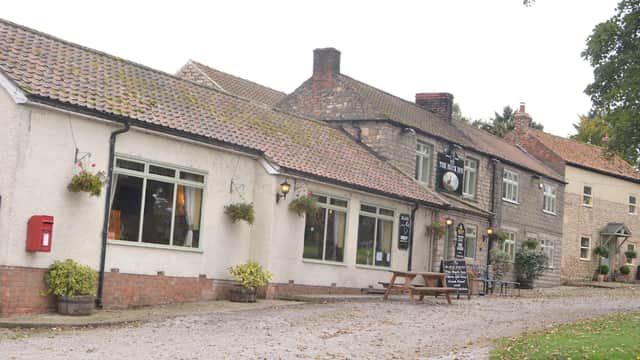Charming Bed & Breakfast with stone and brick exterior, outdoor seating, and flower baskets in a quaint Yorkshire village.
