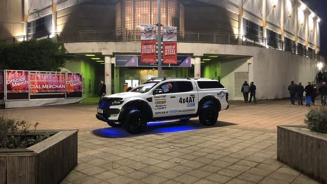 A modified 4x4 vehicle parked near an arena, illuminated with blue lights, showcasing branding for 4x4 Accessories and Tyres.