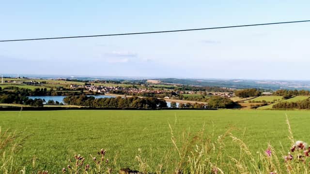 View of lush green fields, a reservoir, and a village in the distance under a clear blue sky in Yorkshire.