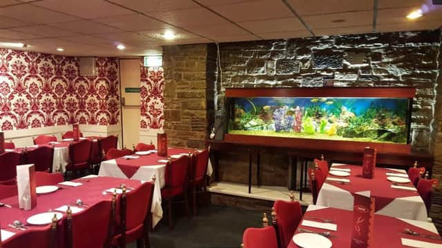 Elegant dining area with red tablecloths, ornate wallpaper, and a large aquarium as a focal point.