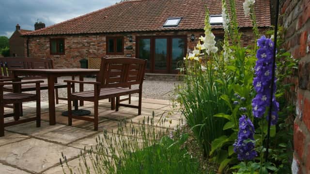 Rustic holiday cottage with a stone patio, wooden seating, and vibrant flowers in West Lutton, Yorkshire.