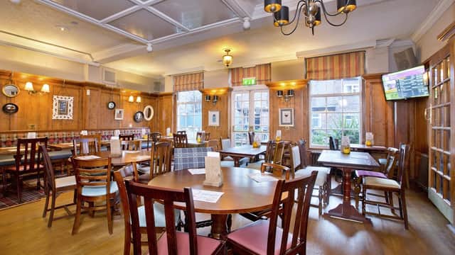 Cozy pub interior with wooden tables, chairs, and warm lighting, featuring large windows and a TV in the corner.