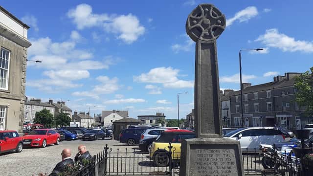 Celtic cross monument in a market square with parked cars and a blue sky in Leyburn, Yorkshire.
