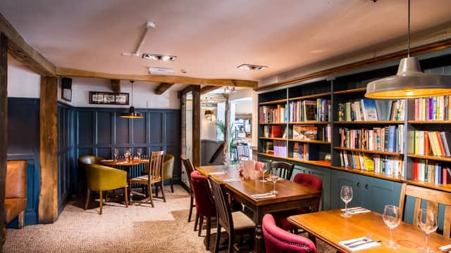 Cozy bar interior with wooden beams, bookshelves, and tables set for dining in Plompton, Yorkshire.