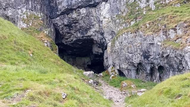 Entrance to Victoria Cave surrounded by rocky cliffs and lush green grass in Langcliffe, Yorkshire.