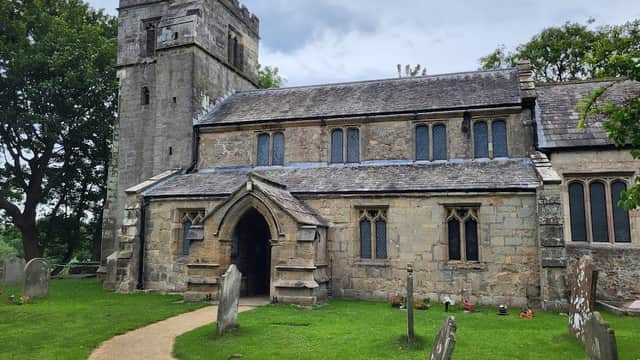 Historic stone church with a tower, arched entrance, and grave markers on a grassy path in Sutton upon Derwent, Yorkshire.